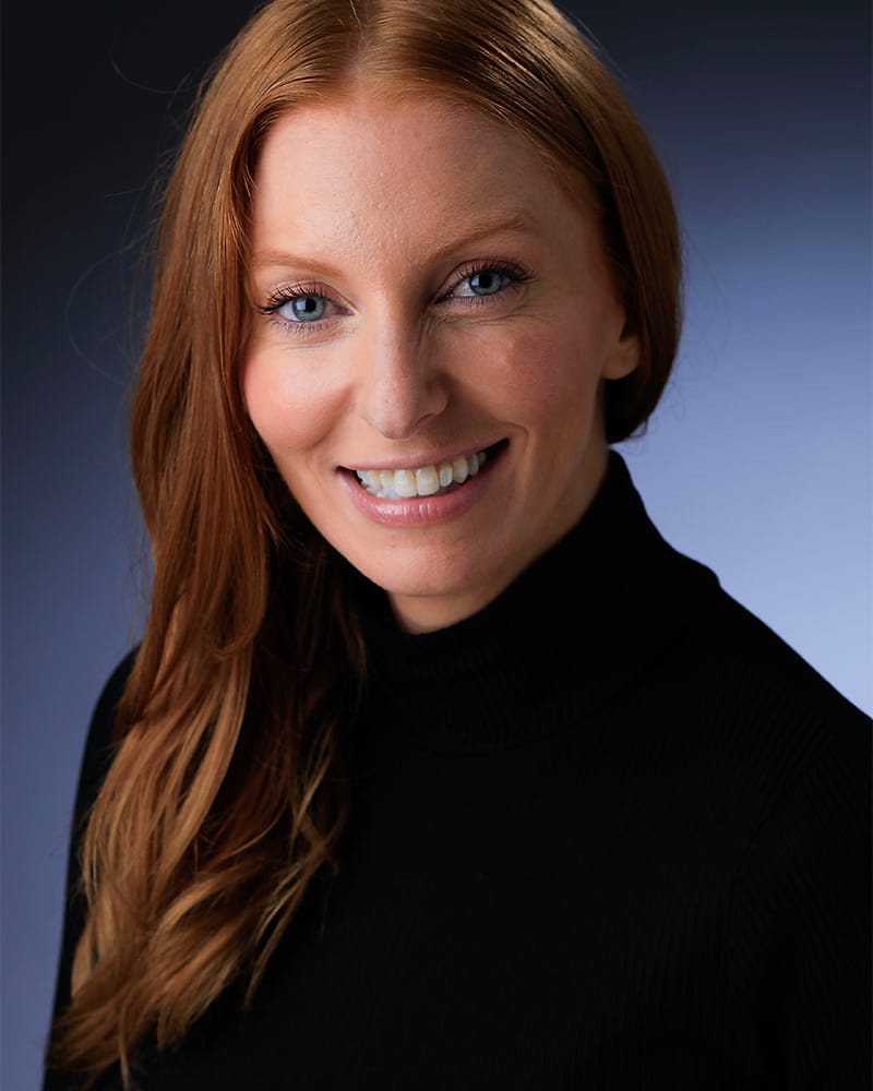 Professional studio headshot of a woman in a black turtleneck on a blue gradient