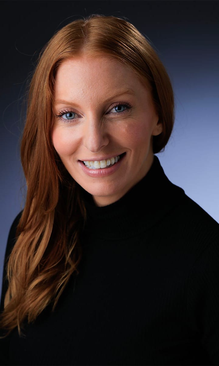 Professional studio headshot of a woman in a black turtleneck on a blue gradient