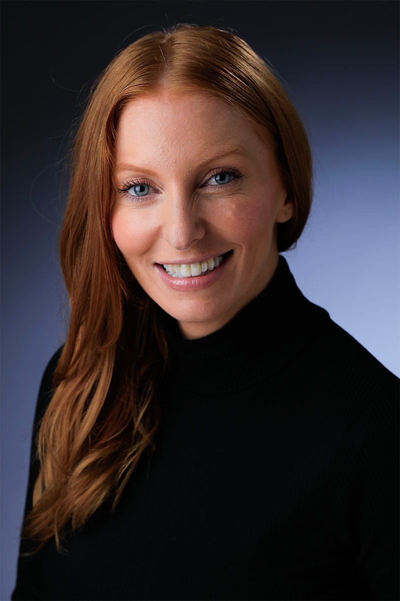 Professional studio headshot of a woman in a black turtleneck on a blue gradient