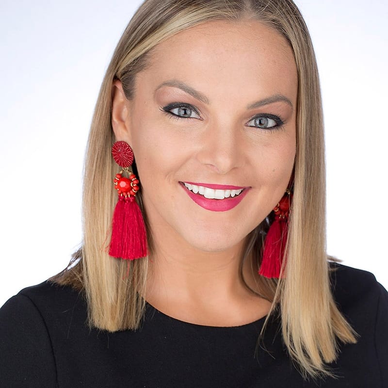 Corporate headshot of a woman in black with red tassel earrings on a white background