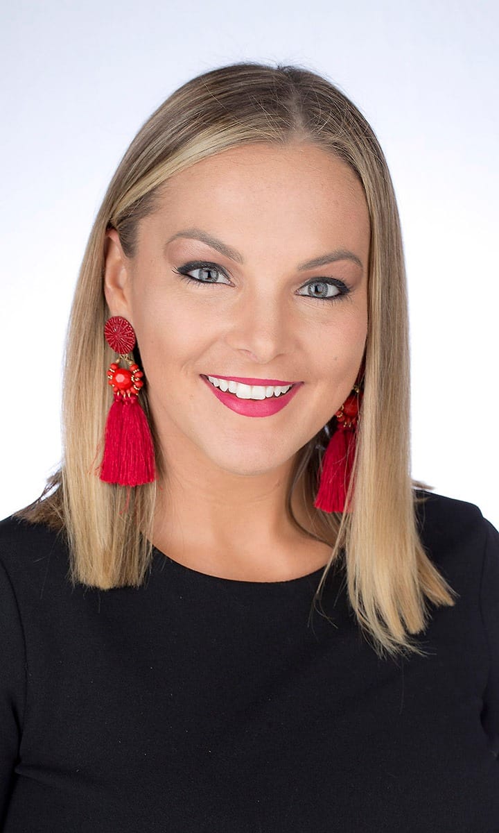 Corporate headshot of a woman in black with red tassel earrings on a white background