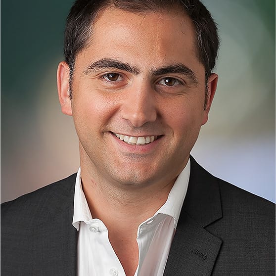 Corporate studio headshot of a man in a dark suit and open-collar white shirt