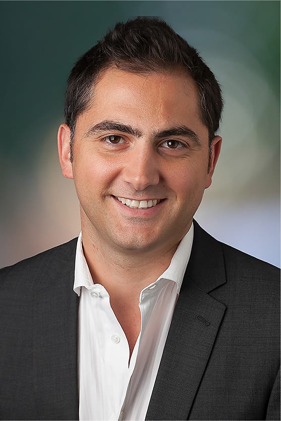 Corporate studio headshot of a man in a dark suit and open-collar white shirt