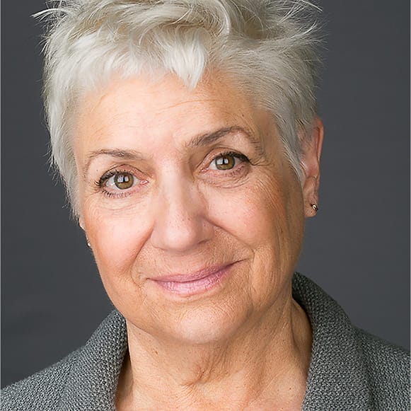 Warm studio portrait of an older woman with short white hair in a gray blazer