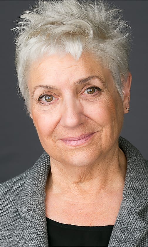Warm studio portrait of an older woman with short white hair in a gray blazer