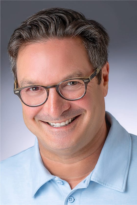 Approachable professional headshot of a man in glasses and a light blue polo