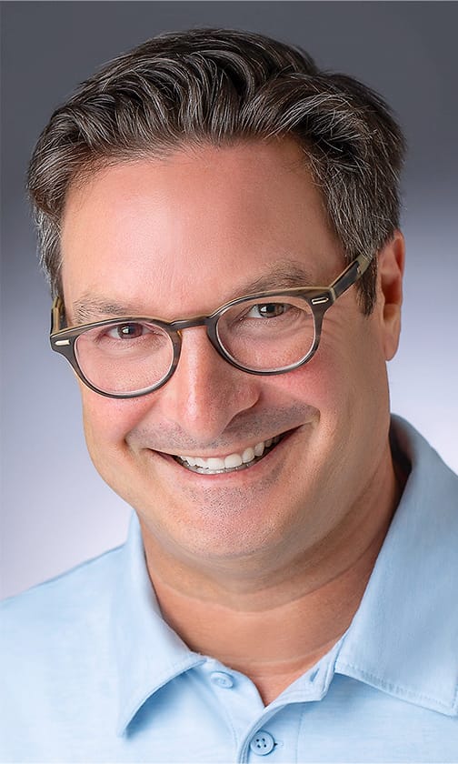Approachable professional headshot of a man in glasses and a light blue polo