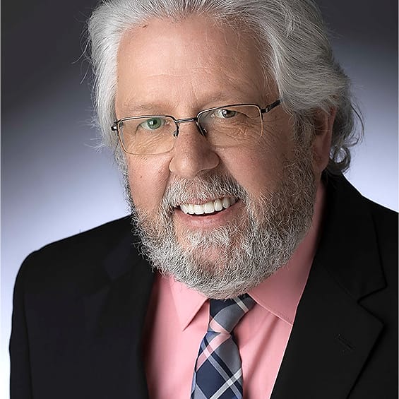 Executive headshot of an older man with white hair and beard in a suit and pink shirt