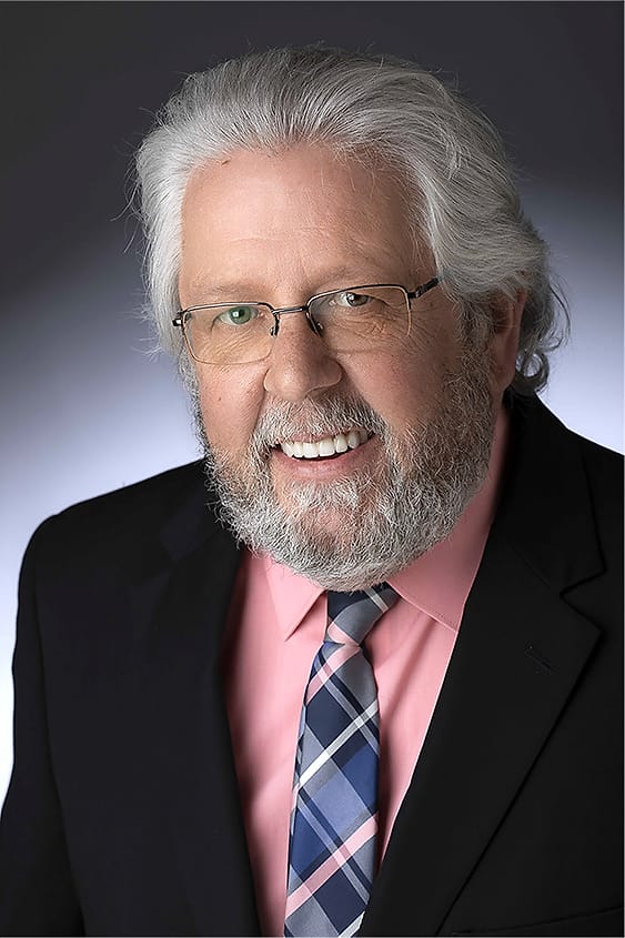 Executive headshot of an older man with white hair and beard in a suit and pink shirt
