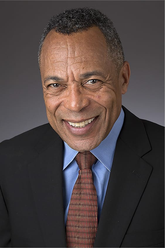 Executive corporate headshot of a man in a black suit, blue shirt, and patterned tie