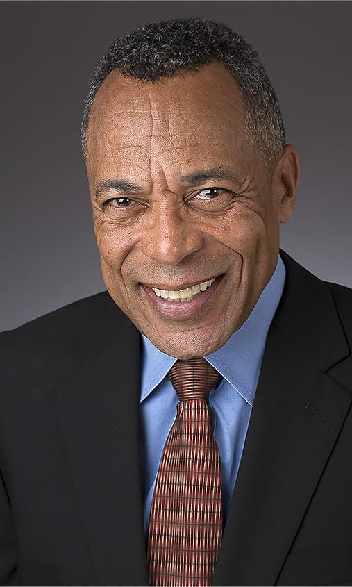 Executive corporate headshot of a man in a black suit, blue shirt, and patterned tie
