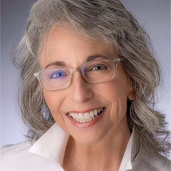 Professional headshot of a woman with gray hair and glasses in a white shirt
