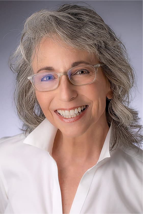 Professional headshot of a woman with gray hair and glasses in a white shirt
