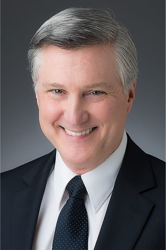 Executive corporate headshot of a man in a navy suit and dotted tie