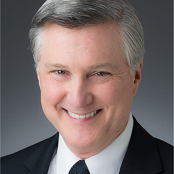 Executive corporate headshot of a man in a navy suit and dotted tie