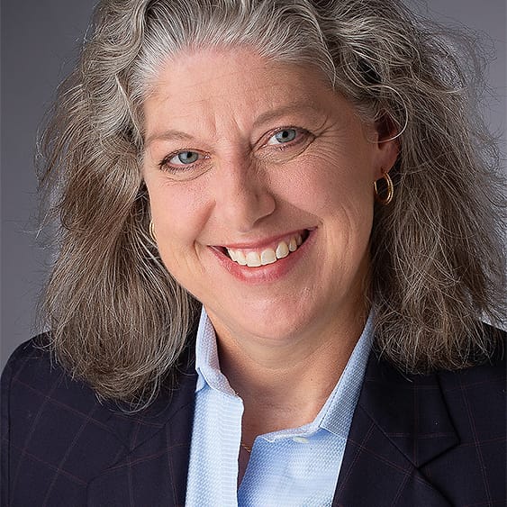 Corporate headshot of a woman with gray hair in a navy windowpane blazer