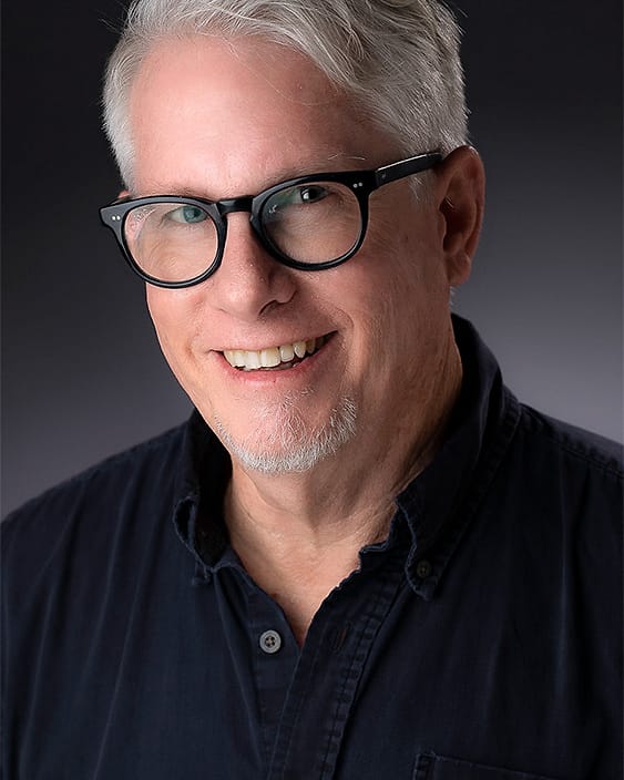 Professional portrait of a man with glasses in a navy button-down
