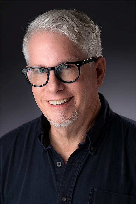Professional portrait of a man with glasses in a navy button-down