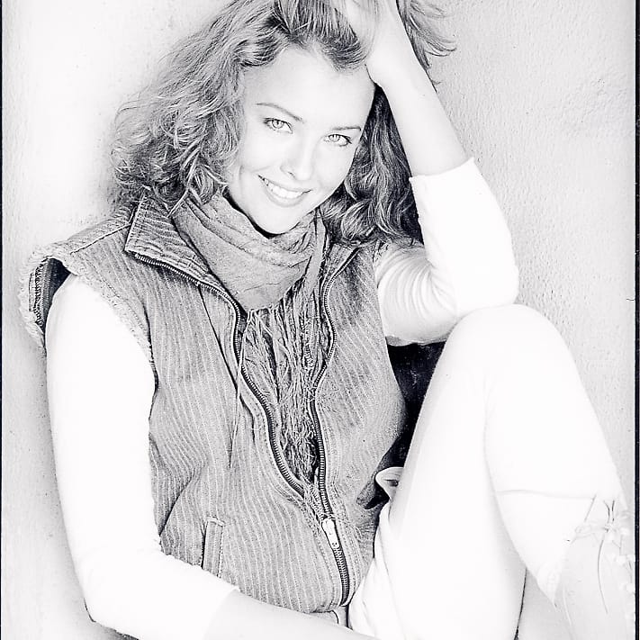 Black and white 1980s-styled creative portrait of a woman seated against a wall