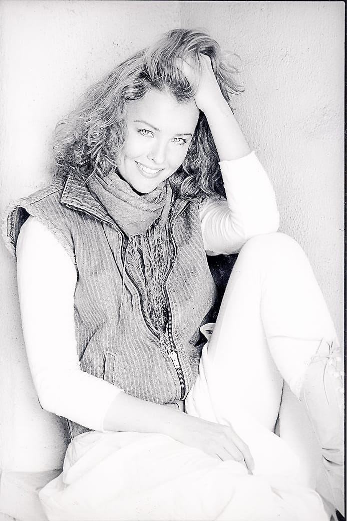 Black and white 1980s-styled creative portrait of a woman seated against a wall